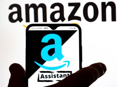 Kiev, Ukraine - January 13, 2022: In this photo illustration, the Amazon Assistant logo is seen displayed on a smartphone screen and Amazon logo in the background. 