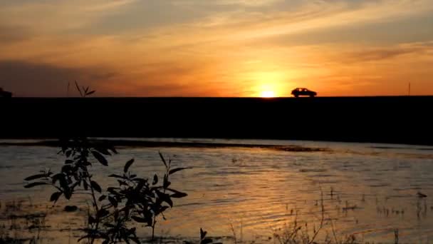 Lago y coches siluetas en la carretera contra la puesta del sol — Vídeo de stock