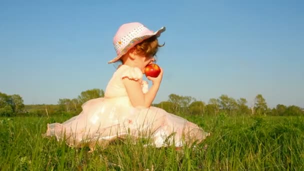 Маленькая девочка ест яблоко на лугу — стоковое видео