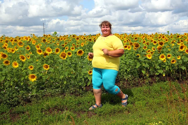 Överviktig kvinna kör längs fält av solrosor — Stockfoto
