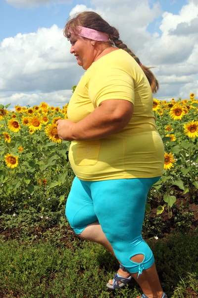 Mulher com sobrepeso correndo ao longo do campo de girassóis — Fotografia de Stock