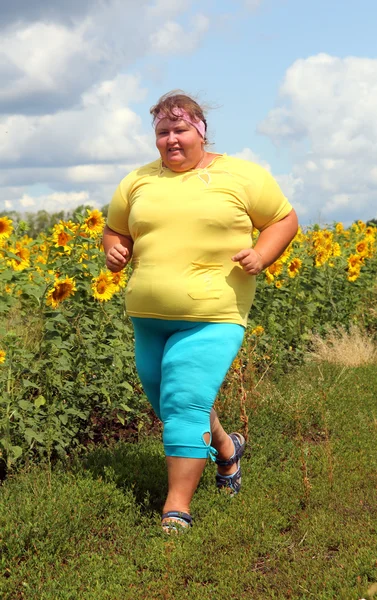 Överviktig kvinna kör längs fält av solrosor — Stockfoto