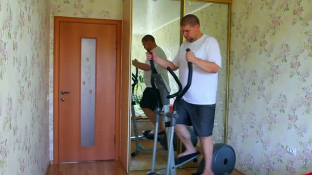 Overweight man exercising on trainer ellipsoid — Stockvideo