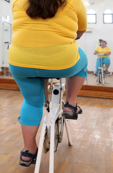 Överviktig kvinna tränar på cykel simulator — Stockfoto