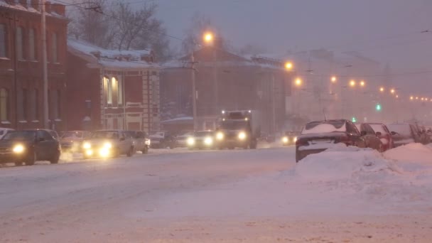 Bilar på en stadsgata i en snöstorm i gryningen — Stockvideo
