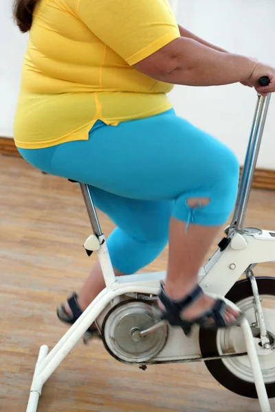 Overweight woman exercising on bike simulator — Stock Photo, Image