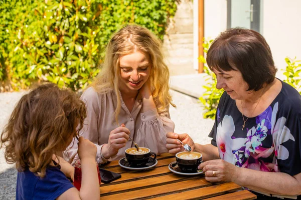 La petite fille avec maman et grand-mère boit du jus dans un café — Photo
