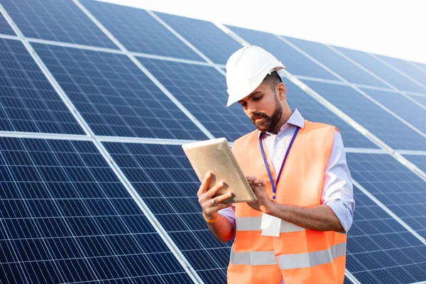 Инженер с планшетом стоит на фоне солнечной станции — стоковое фото