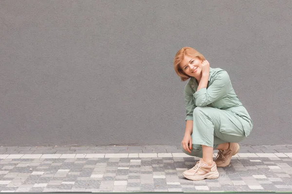 Belle femme accroupi à l'extérieur sur fond de mur gris — Photo