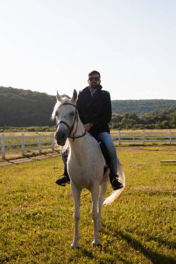 Genç adam bir çiftlikte ata biniyor.