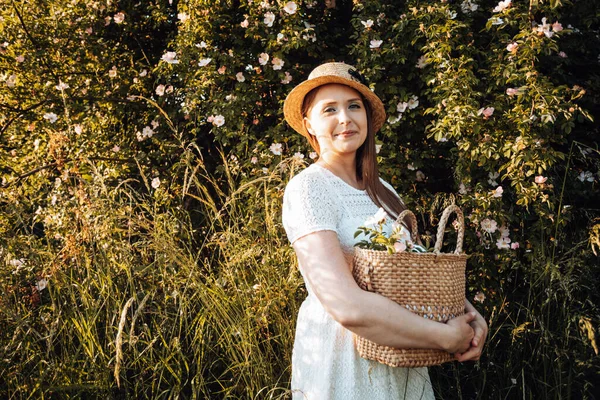 Hübsche Frau mit Hut hält Korb mit Blumen — Stockfoto