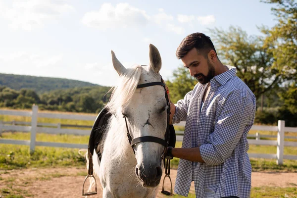 Der glückliche Mann streichelt ein weißes Pferd auf einer Ranch — Stockfoto