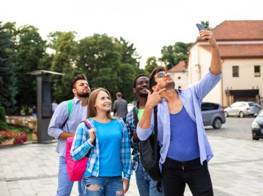 Neşeli bir grup öğrenci dışarıda selfie çekiyor.