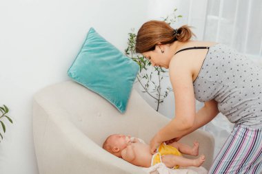 Anne, yeni doğmuş bebeğinin altını sandalyede değiştiriyor.