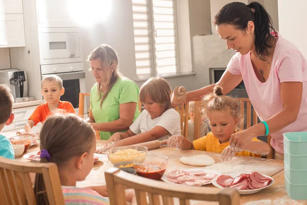 Zwei Frauen mittleren Alters mit kleinen Kindern kochen Pizza — Stockfoto