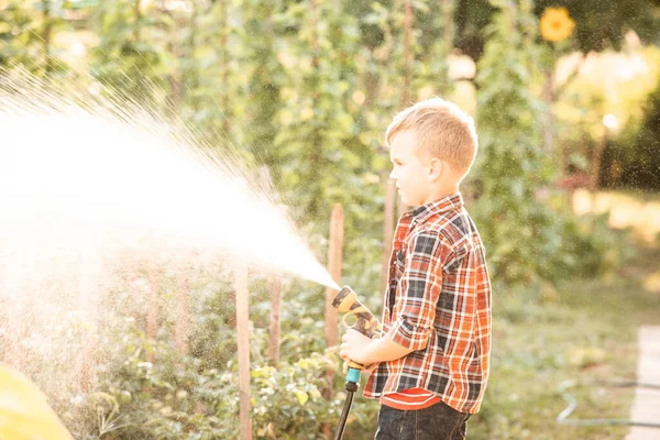 De jongen geeft het tuinbed water met een slang. — Stockfoto