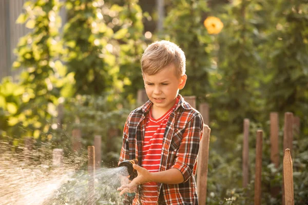 De jongen geeft het tuinbed water met een slang. — Stockfoto
