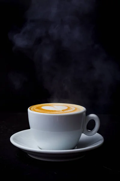 Cappuccino con vapor y amor corazón arte latte en taza blanca en la mesa negra — Foto de Stock