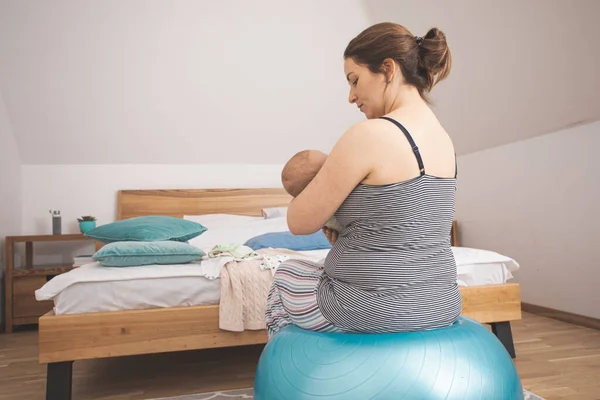Moeder houden en schommelen baby zitten op fitball — Stockfoto