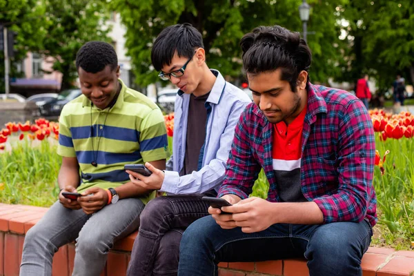 Los hombres jóvenes pierden el tiempo usando aparatos durante la reunión en el parque — Foto de Stock