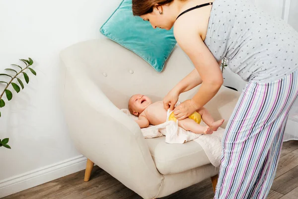 Мать меняет многоразовый подгузник на своем новорожденном ребенке на стуле — стоковое фото