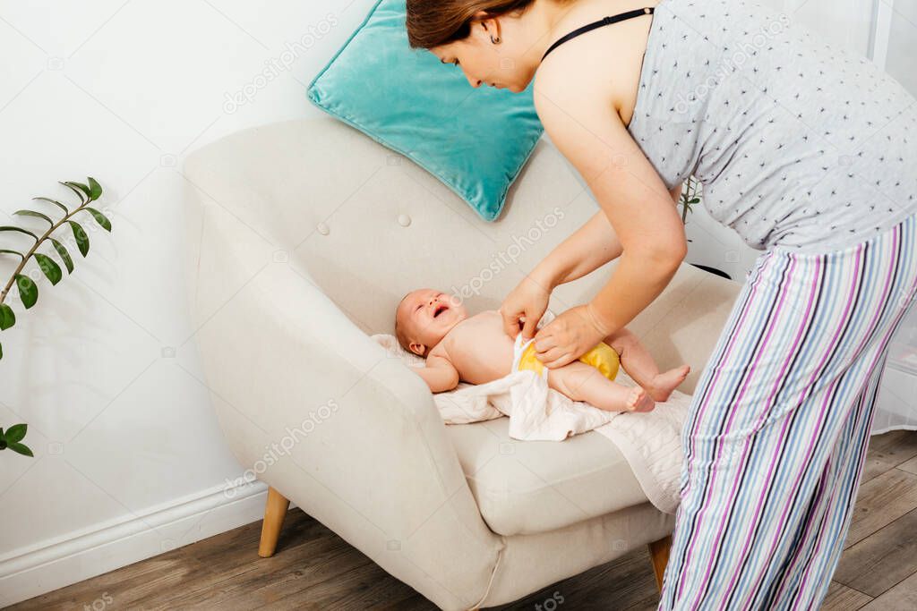 Mother change reusable diaper on her newborn baby on the chair