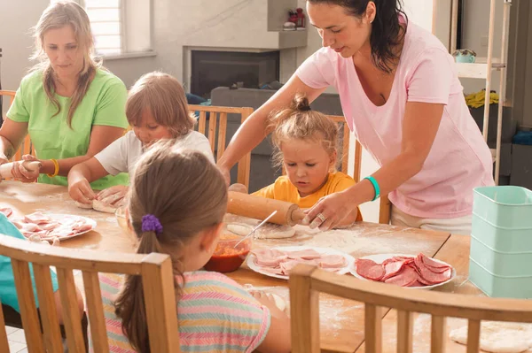 Zwei Frauen mittleren Alters mit kleinen Kindern kochen Pizza — Stockfoto