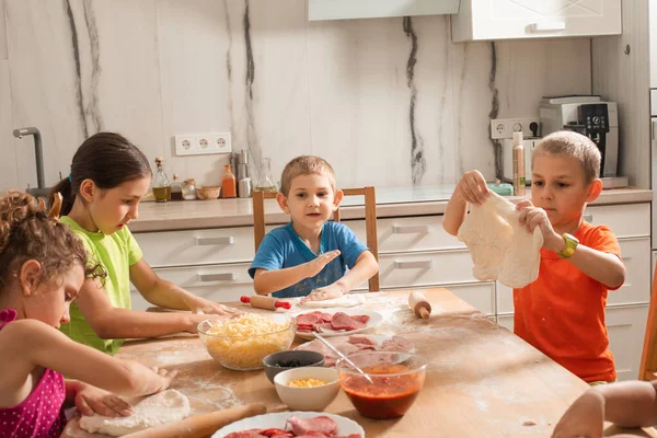 Die niedlichen Kinder sitzen an einem Tisch in der Küche und backen Pizza — Stockfoto