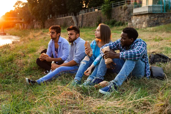 Den grupp unga olika människor som äter snabbmat på naturen — Stockfoto