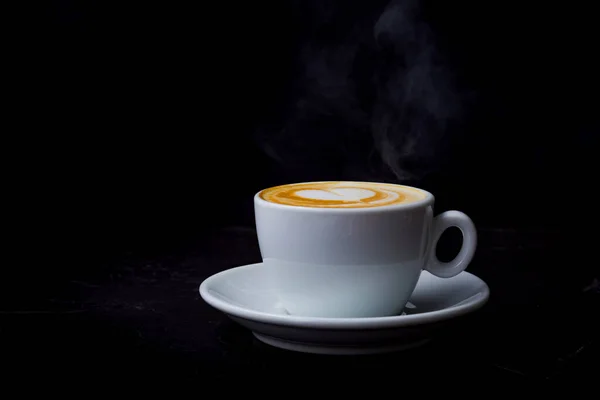 Cappuccino mit Dampf in weißer Tasse auf schwarzem Hintergrund — Stockfoto