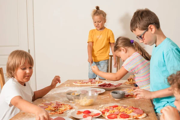 Boldog gyerekek ülnek egy asztalnál a konyhában, és pizzát csinálnak. — Stock Fotó