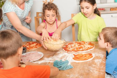 Öğretmeni olan bir grup çocuk pizza hazırlıyor.