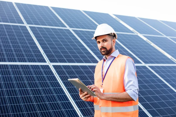 Инженер с планшетом стоит на фоне солнечной станции — стоковое фото