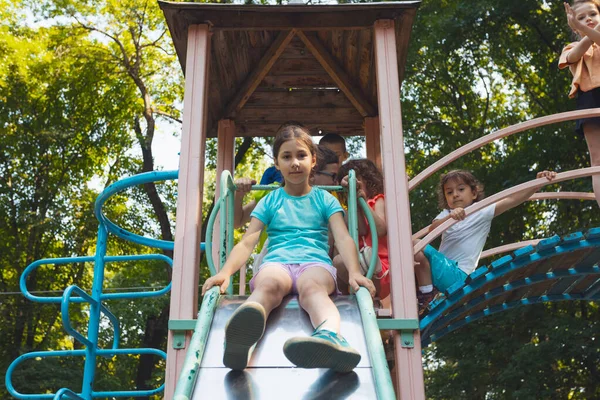 A menina está sentada em um slide no playground — Fotografia de Stock