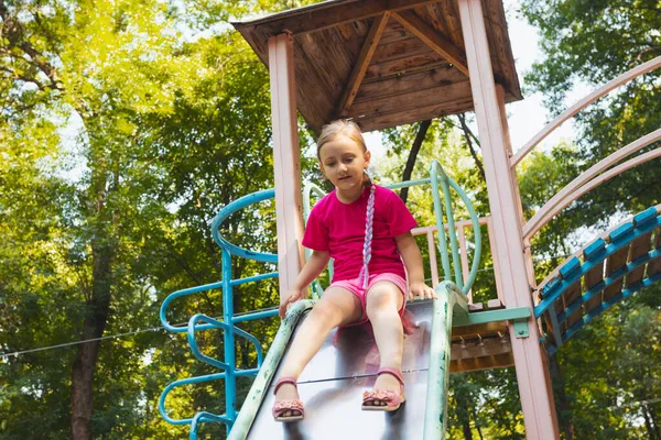 Het kleine meisje zit op een glijbaan in de speeltuin — Stockfoto