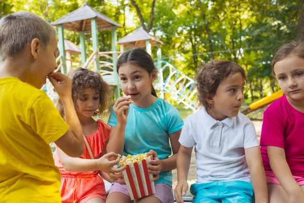 A gyerekek együtt esznek popcornt a parkban. — Stock Fotó