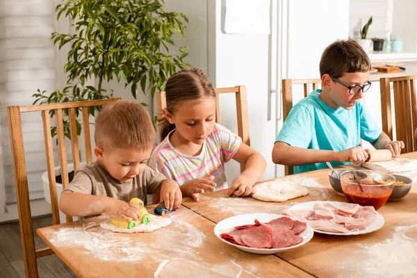 Щасливі діти сидять за столом на кухні і роблять піцу — стокове фото