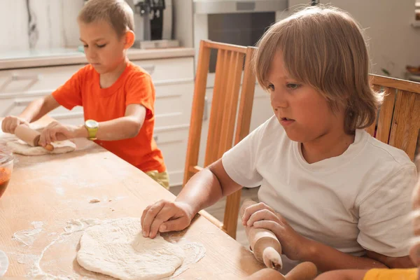 Die Kinder sitzen an einem Tisch in der Küche und backen Pizza — Stockfoto