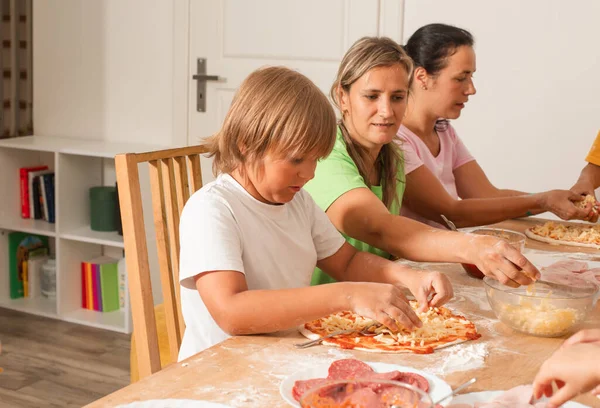 Skupina lidí sedí u stolu v kuchyni a dělá pizzu. — Stock fotografie