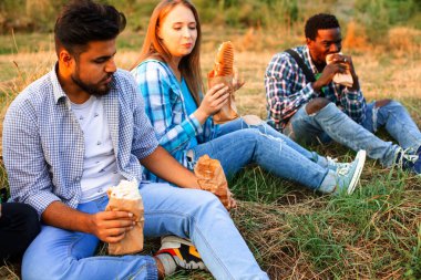 Genç çoklu etnik öğrenciler kampüste fast food yiyorlar.