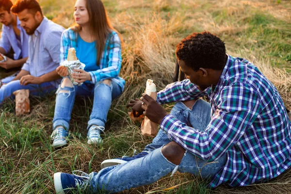 Skupina mladých různorodých lidí, kteří jedí fastfood na přírodě — Stock fotografie