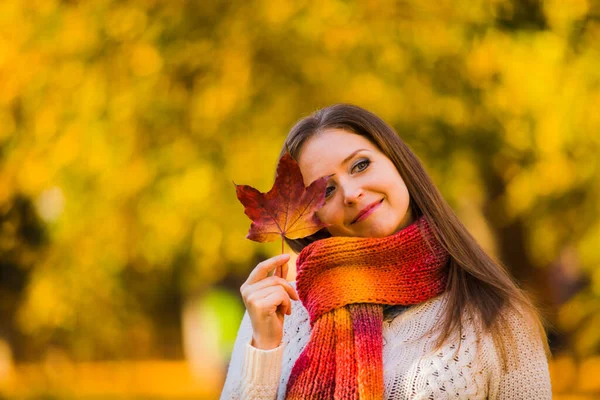 Kobieta w szaliku ukryta z liściem klonu na jesiennym tle — Zdjęcie stockowe