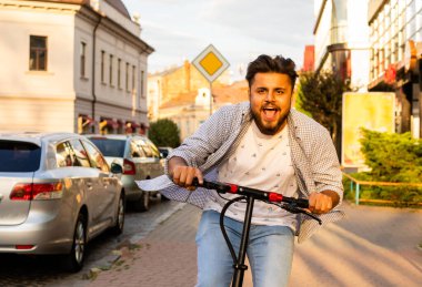Genç adam elektrikli scooter kullanırken iyi bir ruh hali içinde.