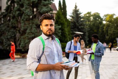 Öğrenci dışarıda durur ve bir yığın kitap tutar.