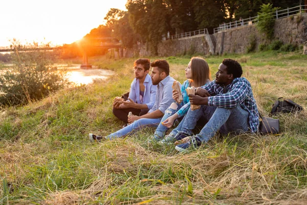 Den grupp unga olika människor som äter snabbmat på naturen — Stockfoto