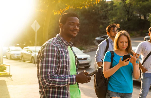 Wielokulturowi studenci ze smartfonami spacerują po mieście — Zdjęcie stockowe