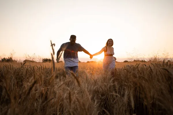 Young adult couple holding hands while walking in field — Stock Photo, Image