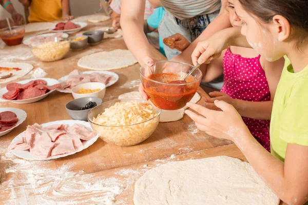 Niños felices se sientan en una mesa en la cocina y hacen pizza —  Fotos de Stock