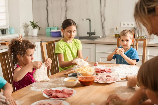 Милые дети сидят за столом на кухне и готовят пиццу. — стоковое фото
