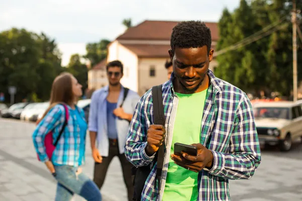 El joven estudiante africano utiliza la navegación en un smartphone — Foto de Stock